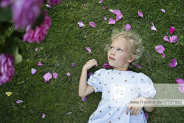 Thoughtful cute girl lying on grass at rose garden