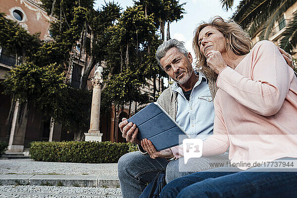 Mature man using tablet PC by thoughtful woman in park