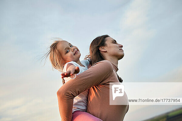 Mother piggybacking cute daughter at sunset