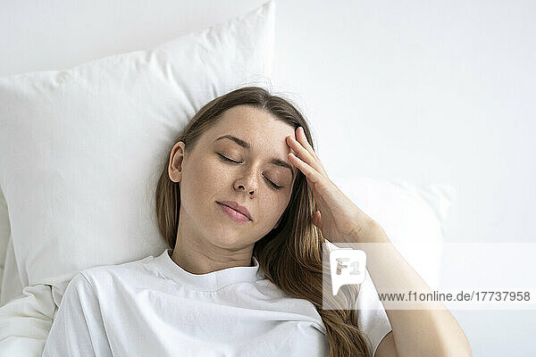 Tired woman with eyes closed lying on bed at home