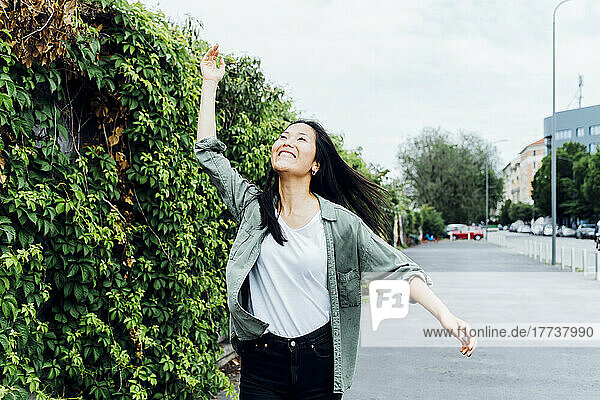 Happy young woman with hand raised enjoying by plants