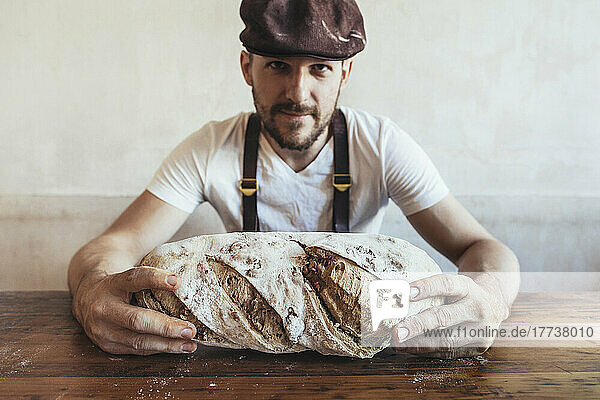 Baker showing freshly baked country bread on table in bakery