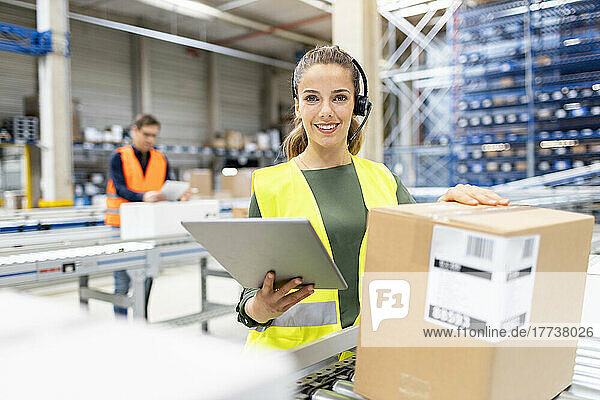 Smiling young worker with tablet PC analyzing cardboard boxes in warehouse