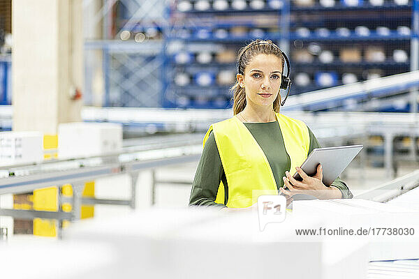 Young worker wearing headset standing with tablet PC in warehouse