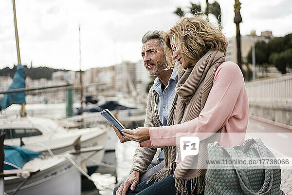 Mature woman reading book by man at harbor