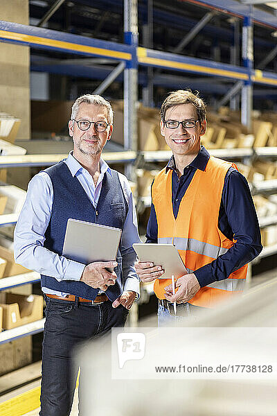 Smiling manager and worker with tablet PC standing in warehouse