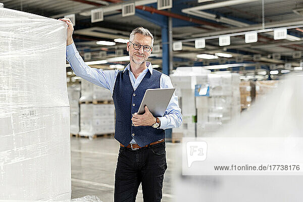 Smiling manager with tablet PC standing by box in warehouse
