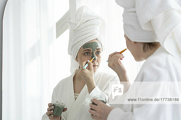 Woman with brush applying facial mask on face at home