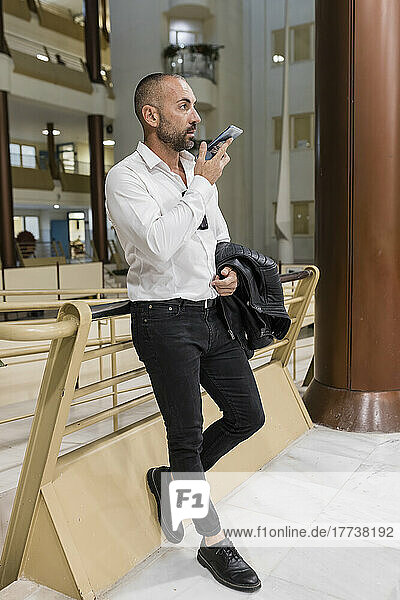 Man talking on speaker phone leaning on railing in hotel