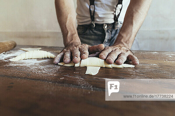 Hände des Bäckers  der Croissants auf dem Tisch in der Bäckerei zubereitet