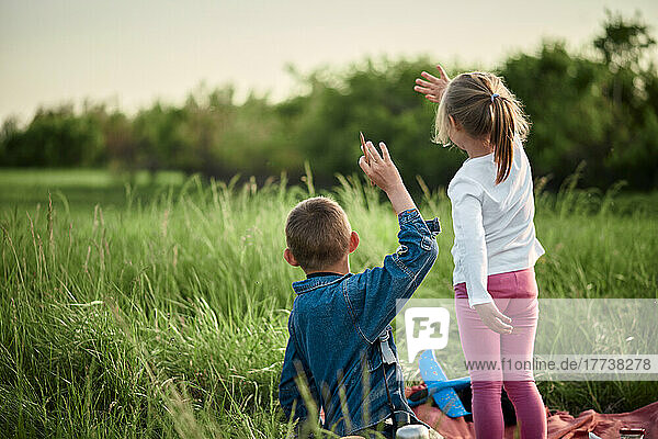 Brother and sister waving hands on field