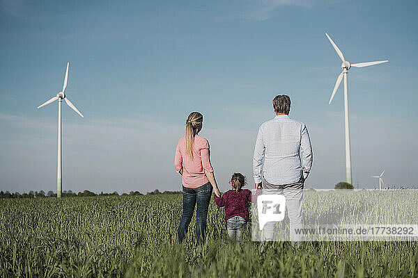 Eltern halten die Hand ihrer Tochter  die an einem sonnigen Tag im Feld steht