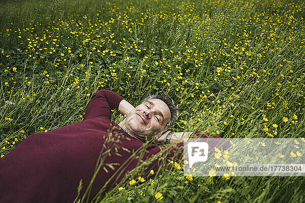 Lächelnder reifer Mann mit den Händen hinter dem Kopf  der auf Gras liegt