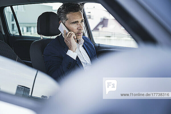 Mature businessman talking on mobile phone sitting on driver's seat in car