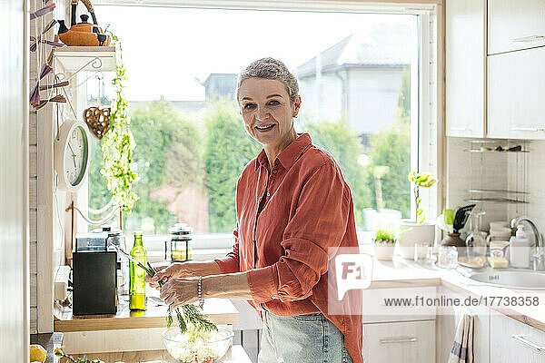 Smiling woman holding herbs in kitchen at home