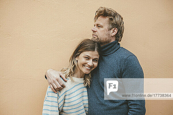 Man embracing woman in front of brown wall