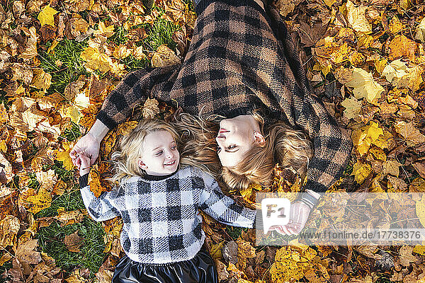 Mother and daughter lying down on autumn leaves at park