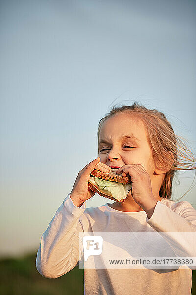 Girl eating sandwich in front of sunset sky