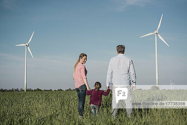 Girl holding parent's hands standing in field on sunny day
