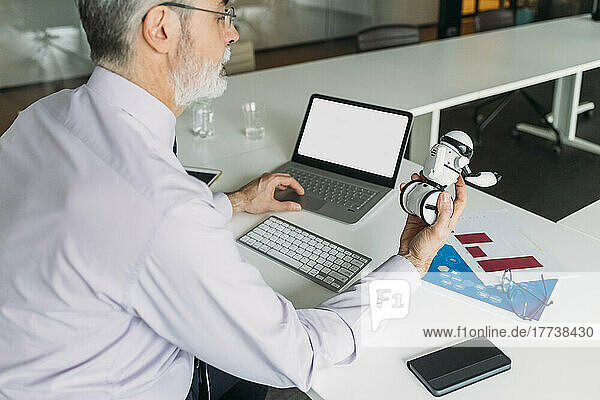Businessman analyzing toy robot sitting at desk in office