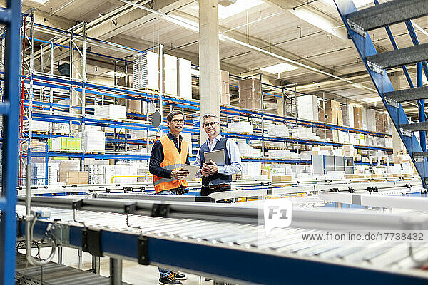 Smiling worker and manager standing with tablet PC in warehouse