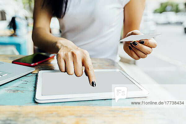 Hands of woman holding credit card making online payment through tablet PC at sidewalk cafe