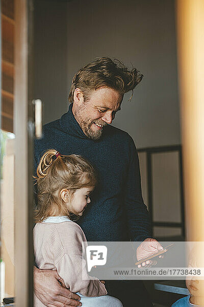Happy man showing mobile phone to daughter seen through window