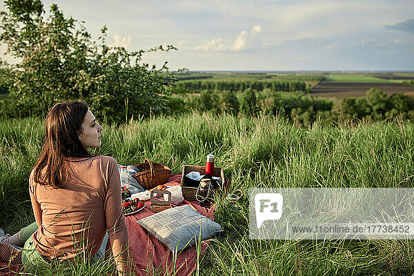 Nachdenkliche Frau sitzt am Wochenende auf einer Picknickdecke im Feld
