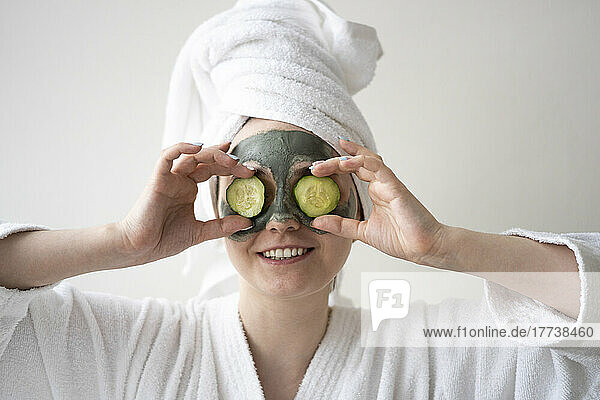 Happy woman holding slices of cucumber over eyes at home