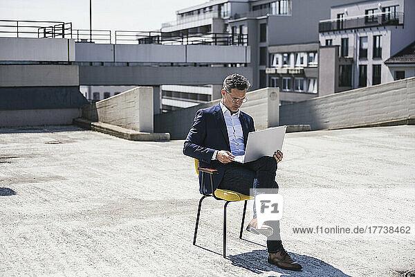 Businessman using laptop sitting on building terrace