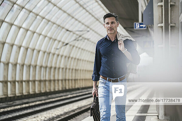Mature businessman carrying bag and jacket walking at railroad station
