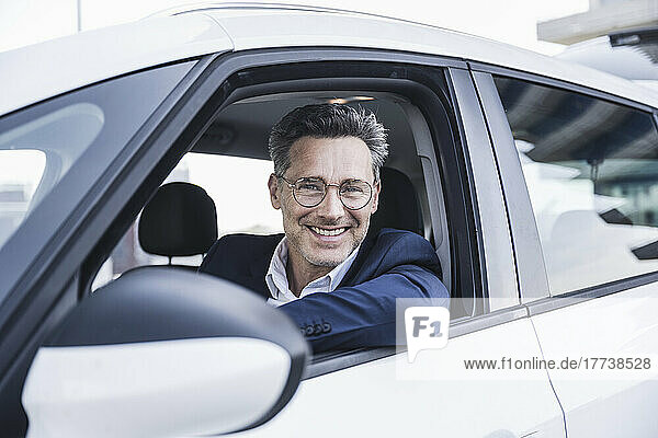 Happy businessman wearing eyeglasses sitting in car