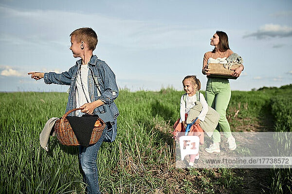 Boy with basket pointing and walking with family in field