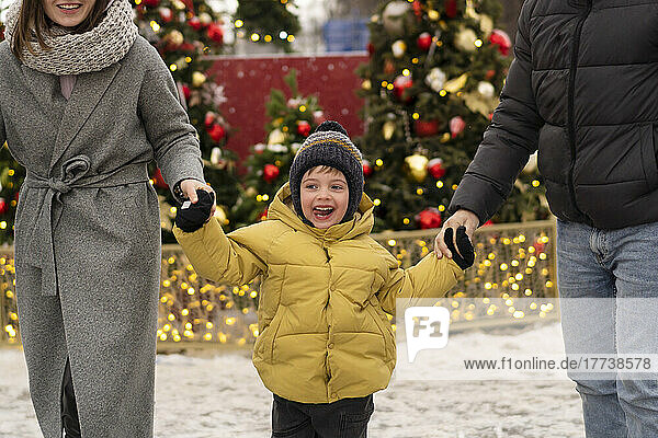 Smiling boy holding hands of parents in Christmas market