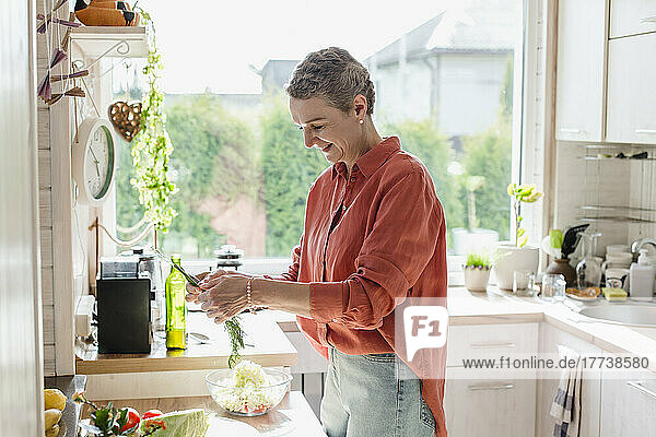 Woman holding herbs for salad in kitchen at home
