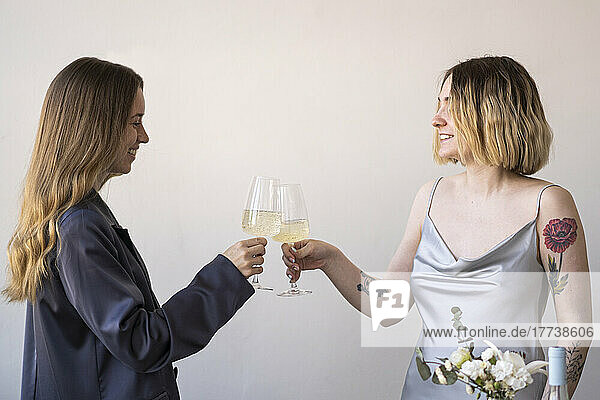 Happy female friends toasting wineglasses in front of wall
