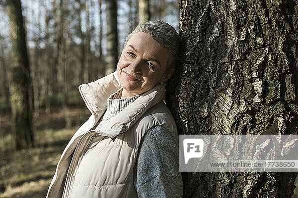 Porträt einer lächelnden Frau  die sich an einen Baumstamm lehnt
