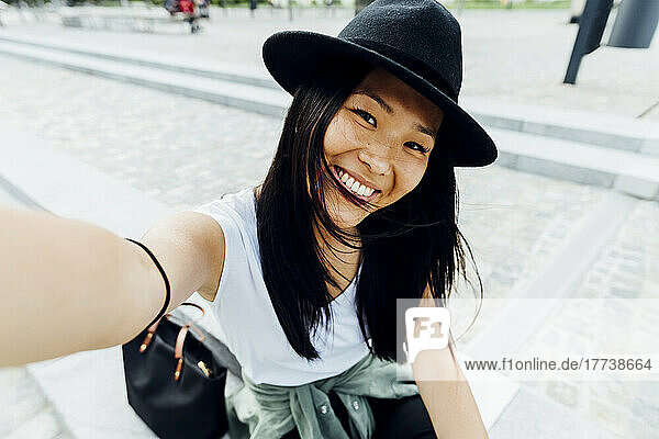 Happy woman with black hair wearing hat taking selfie
