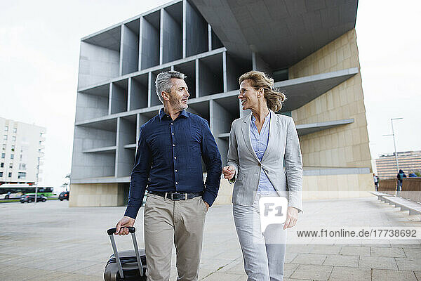 Smiling businesswoman discussing with businessman walking in front of office building