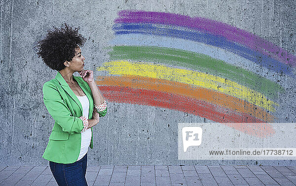 Young woman looking at painted rainbow flag on wall