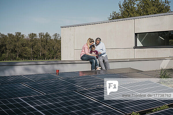 Mann und Frau mit Tochter sitzen an der Wand neben einem Solarpanel