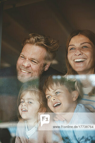 Happy parents and children pressing faces on window glass