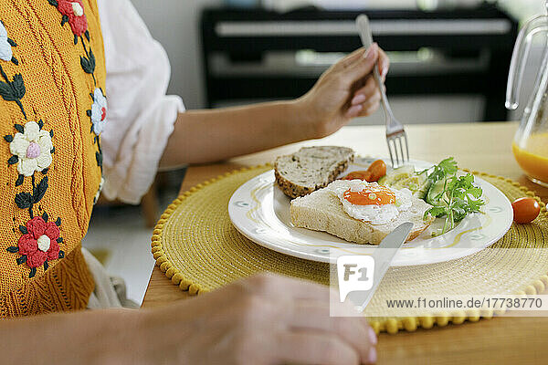 Hands of woman holding table knife and fork by plate on table