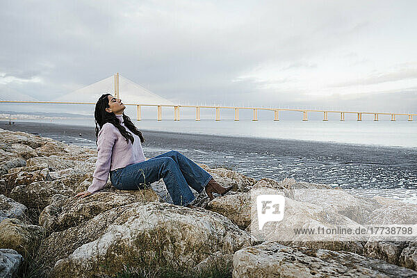 Junge Frau sitzt auf Felsen und entspannt sich am Strand am Fluss