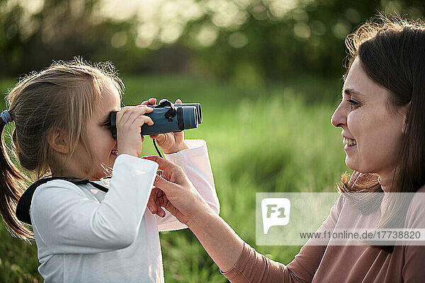 Daughter looking at mother through binoculars in field