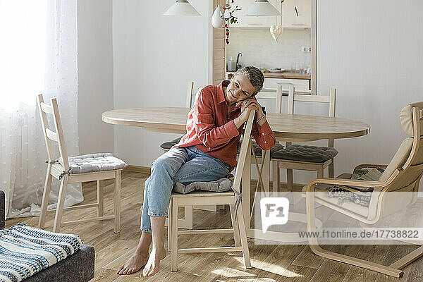 Entspannte Frau sitzt zu Hause auf einem Stuhl am Holztisch