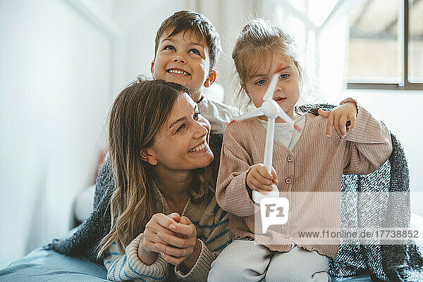 Girl holding wind turbine model sitting by mother and brother