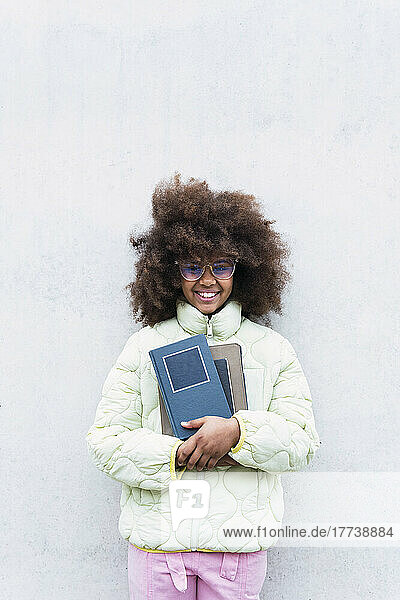 Schoolgirl holding books standing in front of white wall