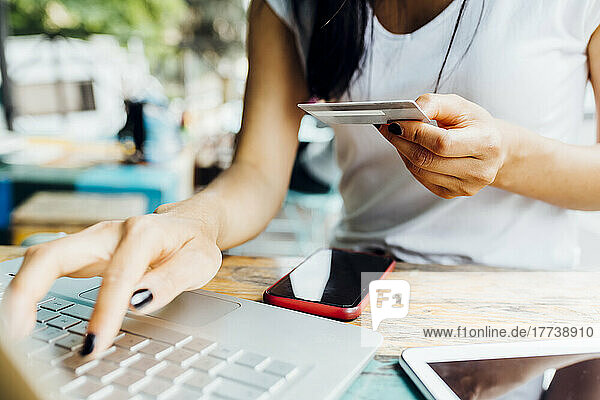 Hände einer Frau  die im Straßencafé eine Kreditkarte am Laptop hält