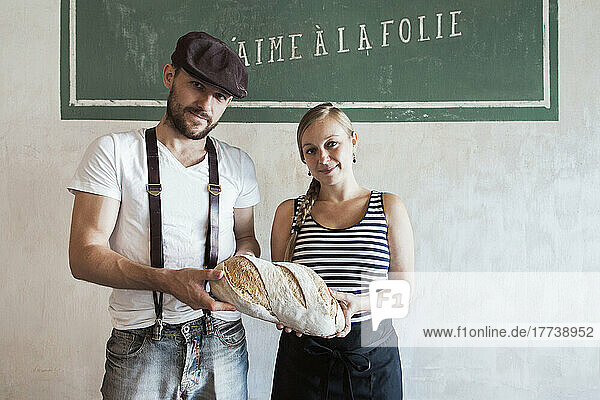 Coworkers holding freshly baked country bread in front of wall in bakery